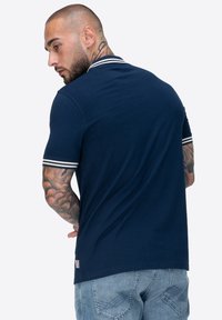 Navyblaues Poloshirt mit weißen gestreiften Kragenakzenten, kurzen Ärmeln und einer schmalen Passform. Hergestellt aus weichem Baumwollstoff mit einer glatten Textur.