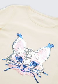 Lichtbeige top met een kattengezicht ontwerp van veelkleurige pailletten in blauw, wit, zilver en roze, met textuurdecoraties.