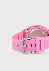 Bracelet de montre en silicone rose avec une boucle en métal argenté, doté d'un design texturé et de plusieurs trous pour un ajustement de taille.