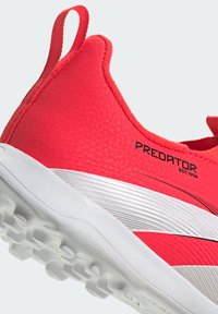 Zapatilla deportiva roja con parte superior texturizada, que presenta una suela blanca y patrones simples. Muestra el mensaje "PREDATOR" y "EST. 1994".