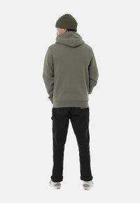 Sudadera de forro polar verde con capucha, combinada con pantalones cargo negros y zapatillas de cuadros sin cordones. Ambientada en un fondo blanco.
