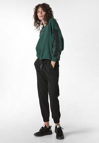 Zelená mikina se černými akcenty; volný střih. Černé zúžené tepláky s bočními kapsami. Černé tenisky dotvářejí celkový vzhled.