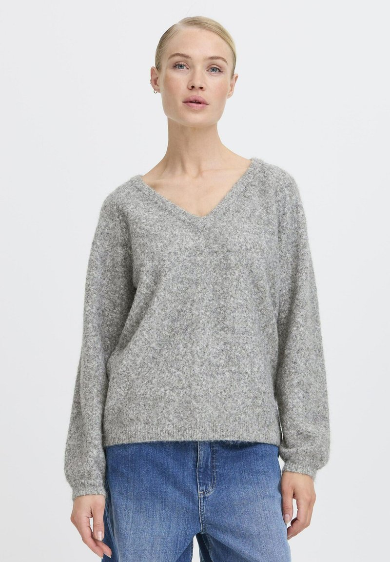 Grauer, weicher Strickpullover mit V-Ausschnitt, langen Ärmeln und lockerem Schnitt. Mit Rippbündchen und -saum, kombiniert mit blauen Jeans.