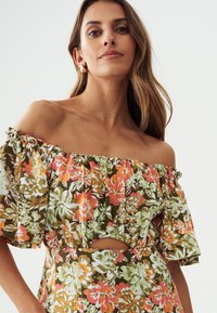Bloemenjurk met off-the-shoulder design, voorzien van een groen, bruin en oranje patroon, met geraffineerde mouwen en een uitsnijding in de taille.