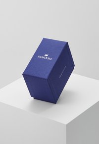 Hexagonal blue gift box with textured surface and the "Swarovski" logo in white on top, placed on a white pedestal.