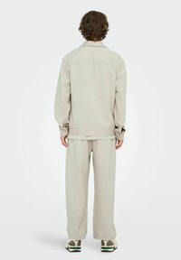 Ensemble beige clair assorti composé d'une veste à manches longues et d'un pantalon à jambes larges, présentant une texture douce et une coupe décontractée.