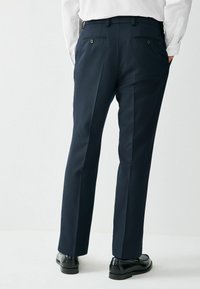 Laivastonsiniset räätälöidyt housut, jotka on valmistettu sileästä kankaasta ja joissa on kaksi takataskua joissa napit sekä laskosyksityiskohdat. Yhdistetty mustiin pukukengiin.