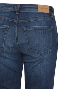 Tmavomodré džínsy z denimu s hladkou štruktúrou, päť vreciek a kožená nálepka na pásovke s nápisom "PULZ JEANS."
