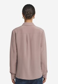 Bluzka z długim rękawem w jasnoróżowym kolorze, z kołnierzykiem, detalem w postaci zakładki z tyłu oraz zapięciem na guziki przy mankietach. Wykonana z gładkiego, lekkiego materiału.