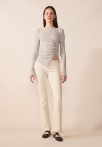 Top gri cu mâneci lungi, cu un design texturat și plisat, având un tiv asimetric, asortat cu pantaloni ajustați de culoare crem și pantofi negri fără toc.