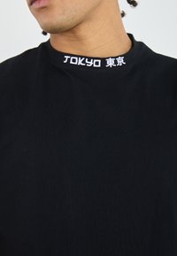 Černé bavlněné tričko s kulatým výstřihem, na límci vyšívané bílé nápisy "TOKYO" a japonské znaky.
