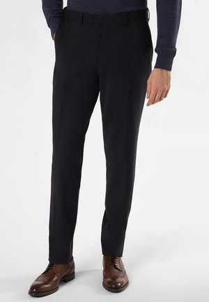 Schwarze maßgeschneiderte Hose mit geradem Schnitt, Ein-Knopf-Verschluss und Taschen, kombiniert mit braunen Brogues. Glatte Stofftextur.