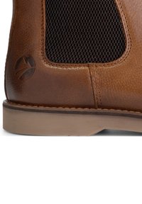 Bruine leren laars met een gestructureerd donker gaaspaneel. Heeft een lichte hak en een logo dat op de zijkant bij de naad is geperst.