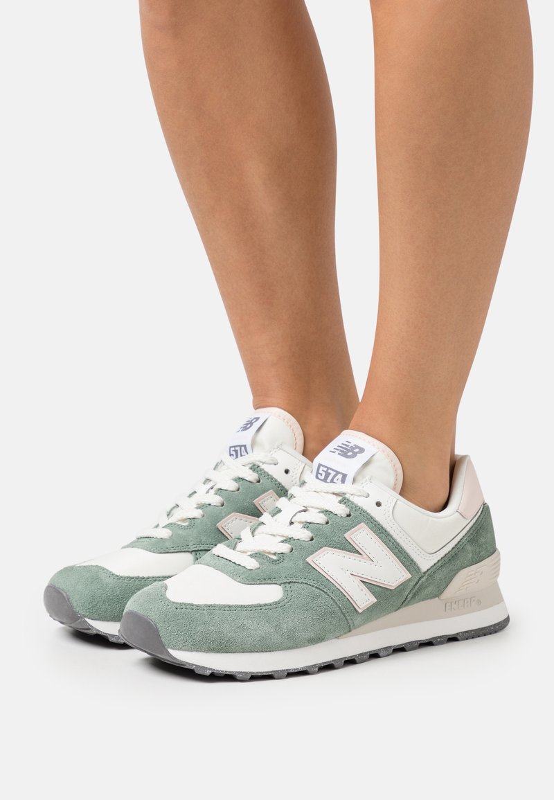 Gröna och vita New Balance 574 sneakers, tillverkade av mocka och läder, med en strukturerad sula, logotypdetaljer och platta skosnören.