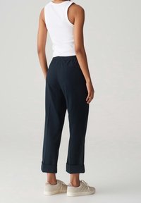 Pantalon marine à coupe décontractée, avec des ourlets à revers et une taille élastique, associé à un débardeur blanc et des baskets de couleur claire.