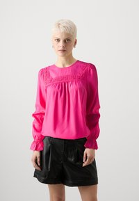 Blusa di un rosa brillante con maniche lunghe e gonfie e uno scollo decorativo ricamato; presenta una vestibilità ampia e una consistenza morbida e liscia.