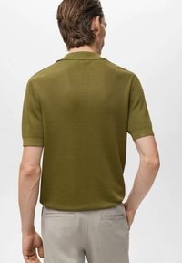 Maslinasto zeleni polo majica s kratkim rukavima, rebrasta tekstura i klasična kragna, u kombinaciji s svijetlosivim hlačama. Vidljiv stražnji pogled.