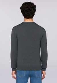 Grauer Pullover mit Rundhalsausschnitt, langen Ärmeln und ribbelten Bündchen. Glatte Textur, taillierte Passform und einfarbig. Getragen mit blauen Jeans.