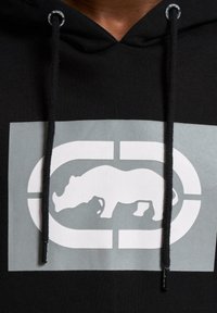 Juodas gobtuvas su didele pilka stačiakampio forma grafika, ant kurios pavaizduota balta raganosio siluetas ir logotipo detalės. Stori raišteliai gobtuve.