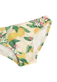 Žlté bikiny s kvetinovým vzorom zelených listov, bielych kvetov a ružových pukov na svetlo béžovej látke, položené na bielom pozadí.