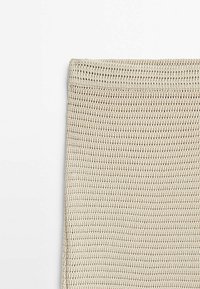 Tissu tricoté beige avec une texture lâche ressemblant à une gauffre, présenté à plat sur un fond blanc.