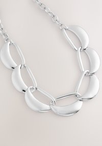 Collier en chaîne de métal argenté avec des maillons ovales et en forme de croissant entrelacés, finition polie et texture lisse.