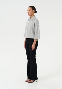 Maglione grigio, corto, con zip e ampio colletto, maniche a tre quarti, abbinato a jeans neri a zampa d'elefante e sandali neri.