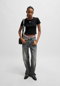 Black cropped t-shirt with logo, paired with loose gray denim jeans featuring a rip, and black ankle boots. Accessories include a small bag.