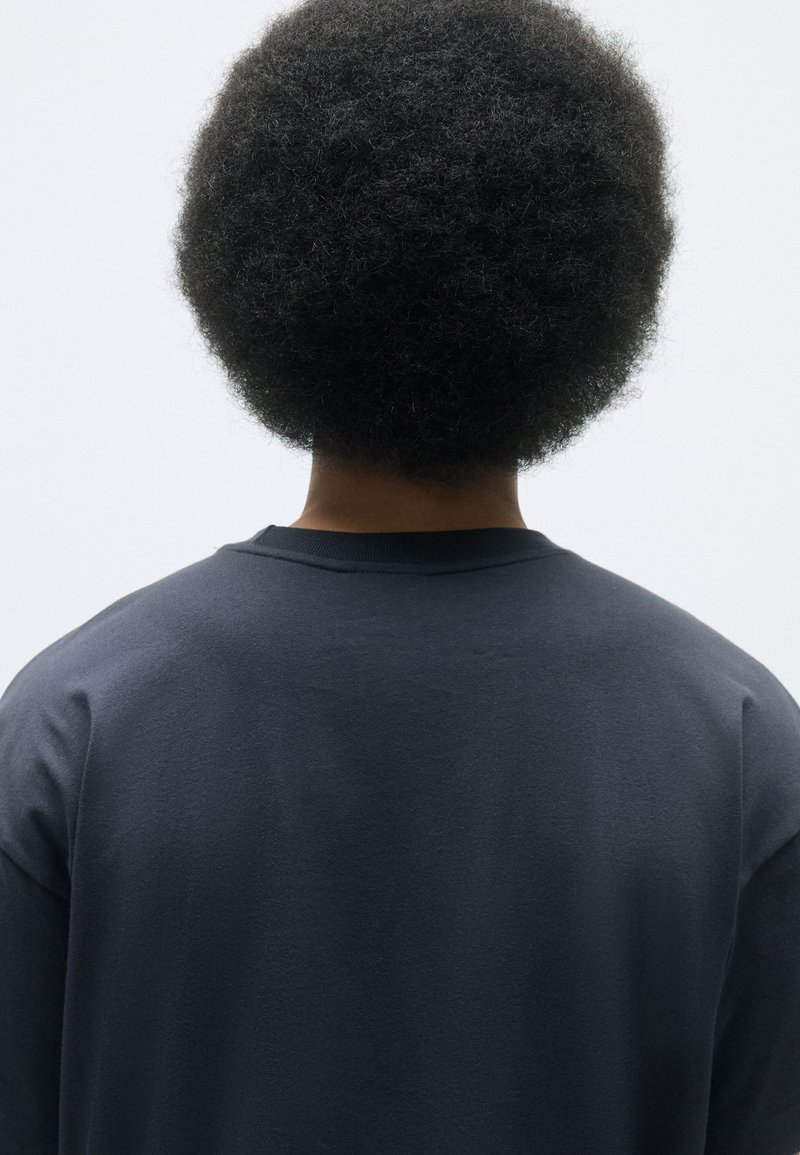 Felpa blu scuro con collo a giro, mostrata dal retro. Presenta una morbida texture in cotone e una vestibilità rilassata. Maniche corte, dettagli minimi.