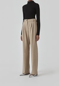 Svart topp med ribbad struktur som bärs tillsammans med högmidjade beige vida byxor, prydda med framfållar och två knappar, kompletterat med blanka silverfärgade skor.