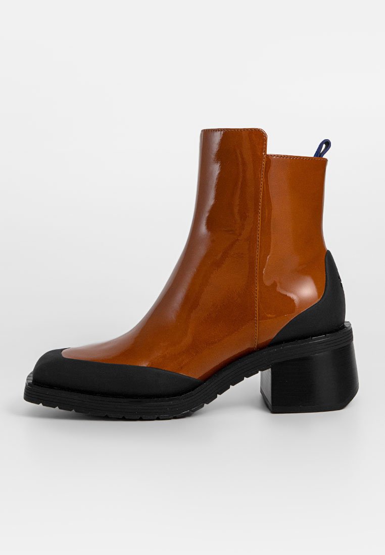 Stiefelette mit glänzendem braunem Obermaterial und schwarzer Gummikappe, ausgestattet mit einem klobigen Absatz und einer Zuglasche hinten für einfaches Anziehen.