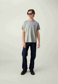 Γκρι κοντομάνικο μπλουζάκι με στρογγυλή λαιμόκοψη, συνδυασμένο με σκούρα μπλε τζιν με λευκές ραφές. Φοριέται με μαύρα γυαλιά ηλίου και παπούτσια.