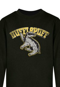 Camisa negra de manga larga con un gráfico de un tejón, con el texto "HUFFLEPUFF" en amarillo arriba, situado sobre la tela oscura de la camiseta.