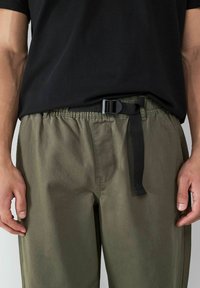 Olijfgroene broek met elastische tailleband en zwarte verstelbare riem. Gemaakt van lichte stof, met een gladde textuur en een relaxte pasvorm.