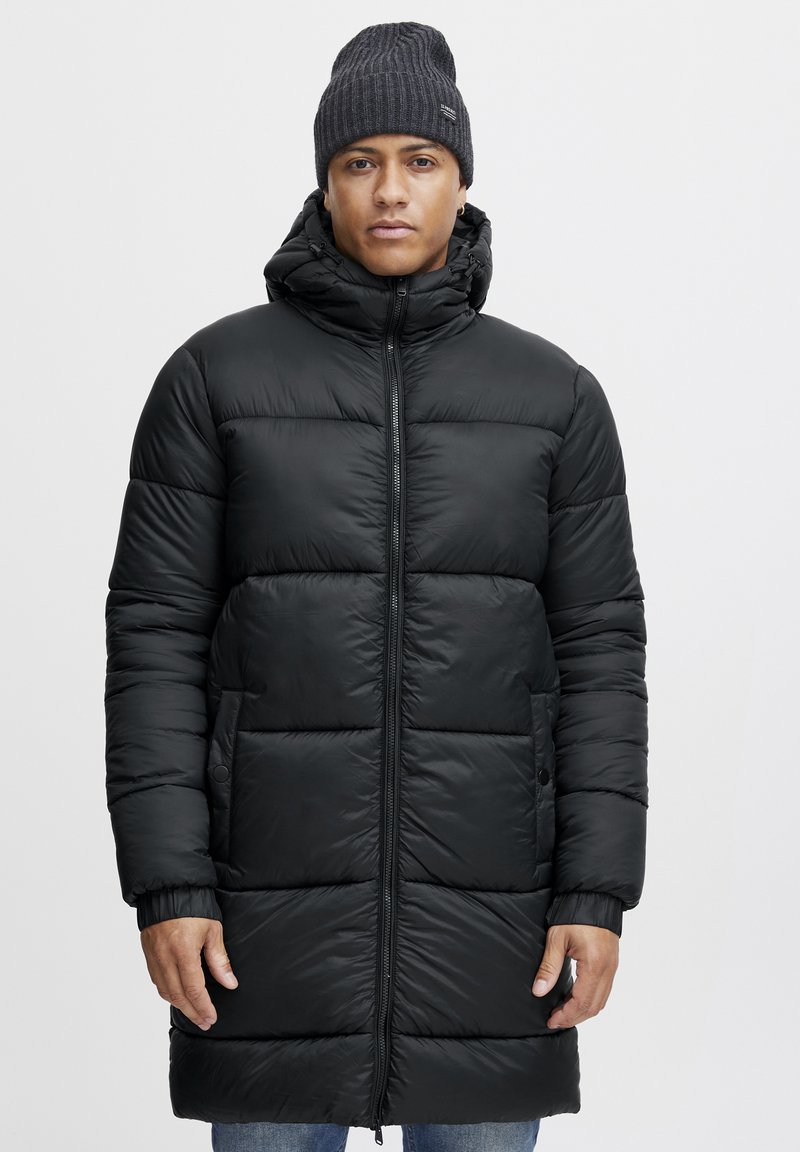 Abrigo puffer negro con capucha, que presenta un diseño acolchado y cierre de cremallera. Puños de canalé, dos bolsillos laterales y una textura suave.