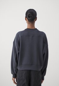 Túlméretezett, sötétszürke pulóver bordás mandzsettákkal és szegéllyel. Puha szövet textúra, amely sima hátoldallal és ejtett vállakkal rendelkezik.