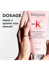Kérastase Genesis conditioner in een lichtroze tube met zwarte en metalen accenten, vastgehouden in een hand met een zilveren ring. Inhoud 200 ml.