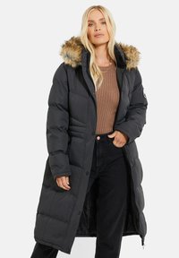 Schwarzer langer Puffer-Mantel mit einer mit Pelz besetzten Kapuze, der über ein gesteppte Design, Frontknöpfe und eine seitliche Reißverschlusstasche verfügt.