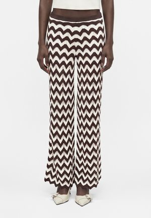 Czarno-białe szerokie spodnie dzianinowe w jodełkę noszone z kremowymi szpilkami z ostrym noskiem i ozdobną klamrą.