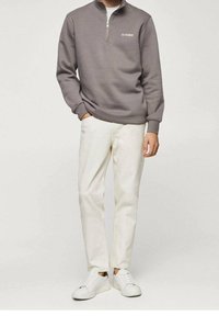 Gray zip-up sweatshirt with "LE STUDIO" text, paired with light beige trousers and white sneakers. Smooth texture and casual design.