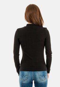 Zwarte geribbelde longsleeve top met een hoge halslijn; gecombineerd met blauwe denim jeans met een kenmerkend ontwerp van de achterzaknaad.