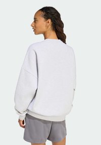 Světlé šedé mikiny s oversized střihem, raglánovými rukávy a žebrovanými manžetami. Materiál vypadá měkce, doplněný tmavě šedými kraťasy.