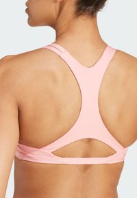 Lichtroze sportbeha met racerback ontwerp, met naadloze stof en uitsnijdingen op de rug voor ademend vermogen.