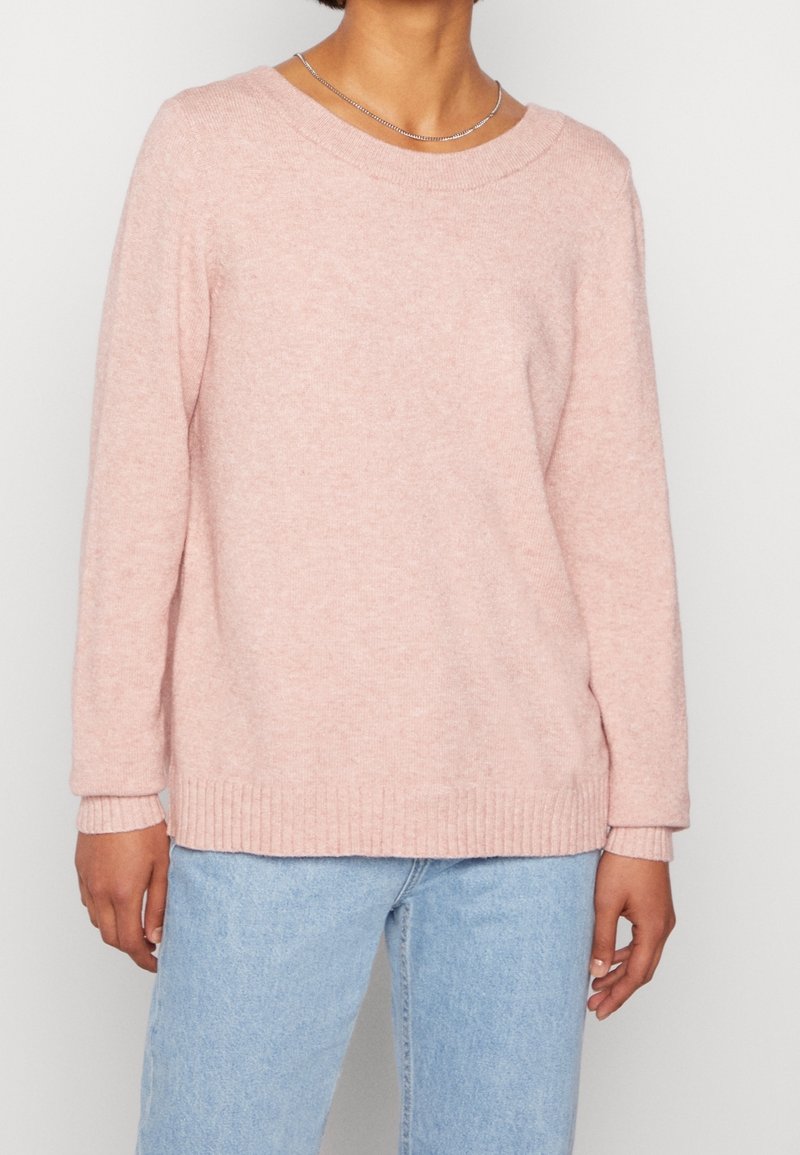 Ljust rosa tröja med långa ärmar, bred halsringning, ribbat nederkant och ärmslut, gjord av ett mjukt, strukturerat tyg. Matchad med ljusblå jeans.