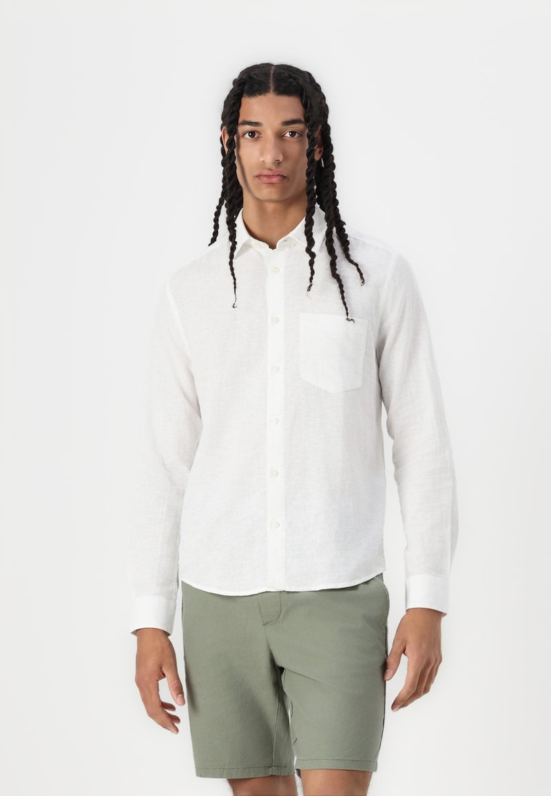 Witte linnen blouse met lange mouwen, knoopsluiting aan de voorkant en een opgestikte zak, gecombineerd met olijfgroene shorts. Soepele textuur, ontspannen pasvorm.