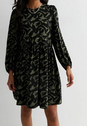Czarna sukienka z rozkloszowanym dołem, zdobiona abstrakcyjnym zielonym wzorem moro, z długimi bufkami na rękawach i marszczoną talią dla dodatkowej objętości.