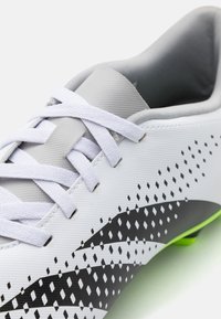 Scarpa da calcio bianca e grigia con upper in sintetico testurizzato, caratterizzata da strisce angolari nere e un motivo a pois, con accentuazioni verdi sulla suola.
