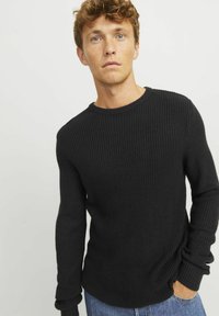 Black ribbed knit sweater with a round neckline, long sleeves, and rolled cuffs, paired with blue denim jeans. Minimalist design.