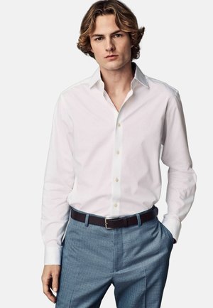 Fehér, hosszú ujjas, gombos ing, hegyes gallérral, világoskék, textúrált öltönynadrággal és sötétbarna övvel párosítva.