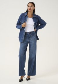 Denimshirt esifriikidega, sinised laiad teksad ja mustad kontsakingad. Riietus sisaldab klassikalist lõiget kontrastsete õmblustega.